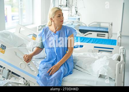 Donna in abito d'ospedale siede sul letto in sala di recupero Foto Stock