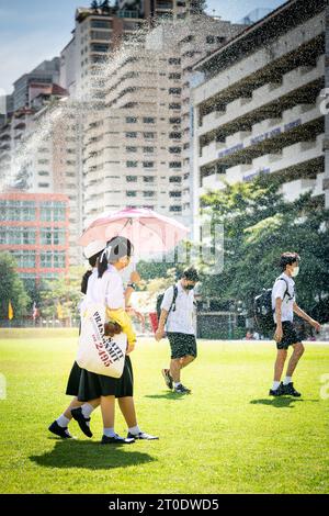 Gli studenti universitari thailandesi vagano attraverso il prato principale dell'Università Srinakharinwirot di Bangkok, Thailandia, e si bagnano dagli irrigatori da giardino. Foto Stock