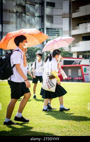 Gli studenti universitari thailandesi vagano attraverso il prato principale dell'Università Srinakharinwirot di Bangkok, Thailandia, e si bagnano dagli irrigatori da giardino. Foto Stock