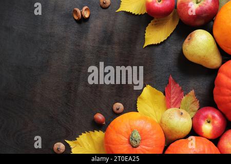 Sfondo autunnale con zucche mature, mele, pere, foglie cadute e ghiande. Vendemmia autunnale su sfondo di legno scuro, vista dall'alto. Giorno del Ringraziamento Foto Stock