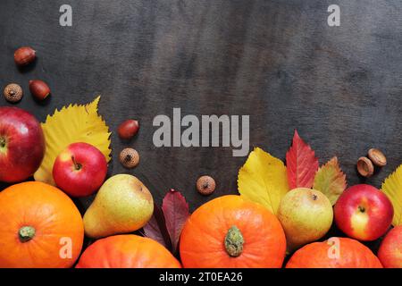 Sfondo autunnale con zucche mature, mele, pere, foglie cadute e ghiande. Vendemmia autunnale su sfondo di legno scuro, vista dall'alto. Giorno del Ringraziamento Foto Stock