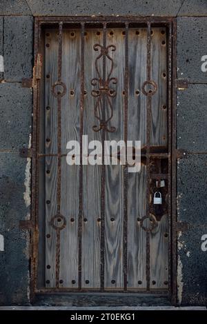 Porta di legno chiusa dietro la griglia arrugginita a Lanzarote, Spagna Foto Stock