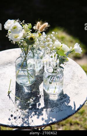 Due mazzi di fiori estivi in piccoli vasi di vetro su un tavolo rotondo all'aperto Foto Stock