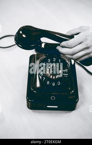 La mano femmina afferra il ricevitore di un vecchio telefono con cavo Foto Stock