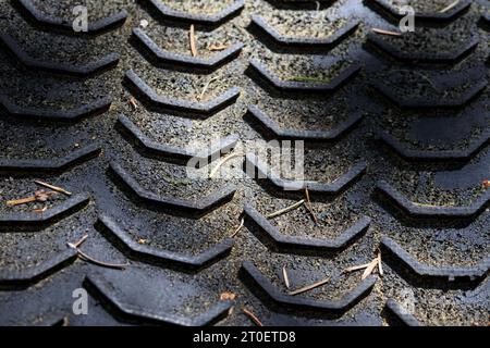 Struttura astratta del tappetino in gomma nera nella foresta, primo piano. Schema delle filettature degli pneumatici sfocato. Sfondo del percorso mountain bike. Tappetino per filettature lunghe in gomma Foto Stock