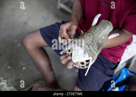 Uomo del posto, creatore di maschere, che lavora su una nuova maschera tradizionale sull'isola Majuli ad Assam, in India Foto Stock