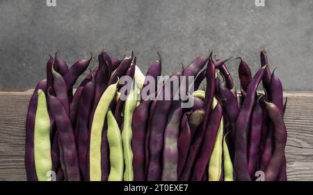 Fagioli sul tavolo. Sfondo di raccolta vegetale o concetto di giardinaggio autunnale. Vista dall'alto di lunghi fagioli viola e gialli crudi su una tavola di legno. Varietà di Purpl Foto Stock