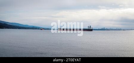 Le navi da carico ancorate fuori dal centro città di mattina presto. Paesaggio marino panoramico con navi container, skyline della città e montagne. Selectiv Foto Stock