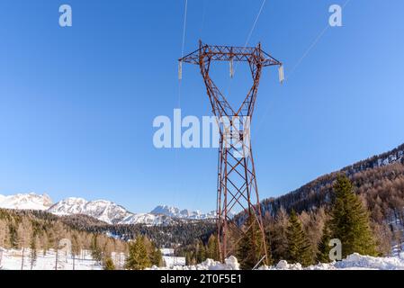 Tralicci elettrici in metallo in un paesaggio innevato di montagna in una chiara giornata invernale Foto Stock