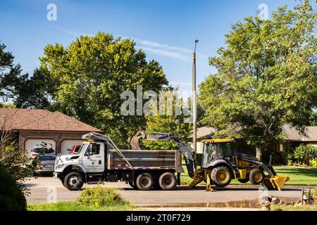 Un dipendente del dipartimento idrico di Wichita, Kansas, scava una linea d'acqua con il retroescavatore John Deere con il bulldozer in un quartiere urbano. Wichita, Kansas, USA. Foto Stock