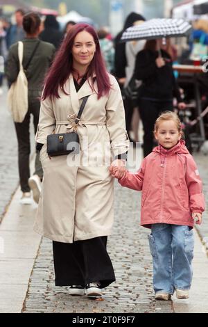 Una giovane donna sorridente con sua figlia sta camminando lungo il lungomare in una giornata autunnale piovosa, tra gli altri pedoni. Foto Stock