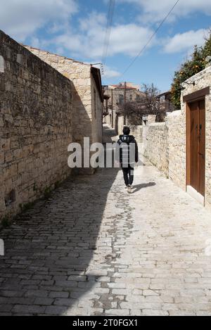 Persona non riconosciuta che cammina su un sentiero in pietra che attraversa un villaggio tradizionale. Case in pietra con porte in legno. Foto Stock