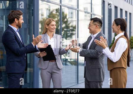 Colleghi team aziendale applaudendo e salutando colleghi donne capo, persone soddisfatte sostengono il capo fuori dall'edificio degli uffici, gruppi eterogenei di uomini d'affari. Foto Stock