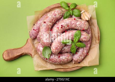 Tavola con salsicce crude fatte in casa, foglie di basilico e grani di pepe sul tavolo verde, vista dall'alto Foto Stock