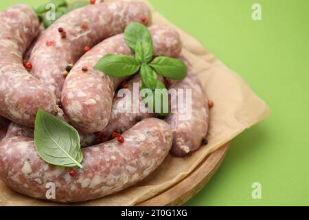 Tagliere con salsicce crude fatte in casa, foglie di basilico e grani di pepe su tavola verde, primo piano. Spazio per il testo Foto Stock