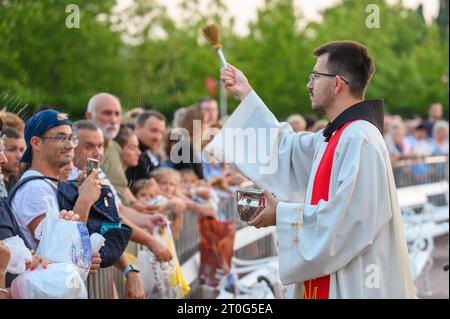 Un sacerdote che benedice gli articoli religiosi dei fedeli dopo la Santa Messa di sera a Medjugorje. Foto Stock