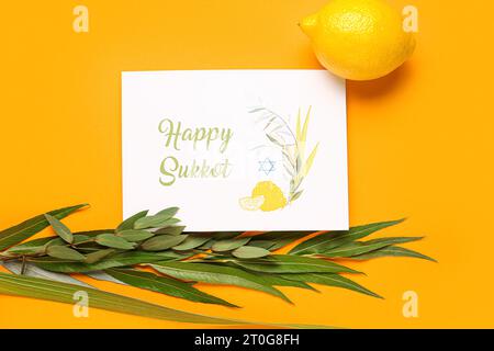 Quattro specie (lulav, hadas, arava, etrog) e biglietto d'auguri con testo HAPPY SUKKOT su sfondo arancione Foto Stock