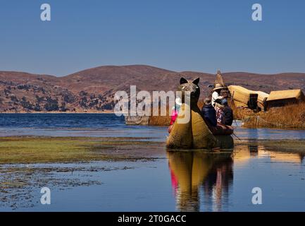 Uomo Uros che trasporta turisti su una barca a canne vicino alla sua isola galleggiante sul lago Titicaca Foto Stock