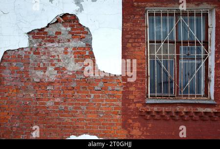 Finestra protetta con griglia di ferro in metallo arrugginito su vecchia parete di mattoni grunge rossi con intonaco bianco caduto Foto Stock
