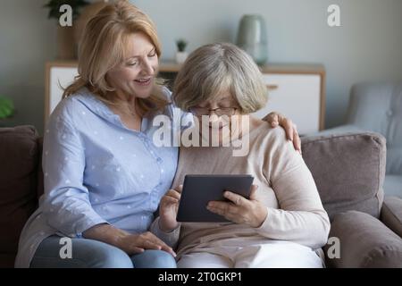 Figlia matura felice che insegna a mamma anziana a usare l'app online Foto Stock