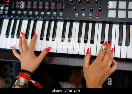 Vista dall'alto delle mani dei Red Nails di un pianista o tastierista di una Rock Band che suona un sintetizzatore Foto Stock