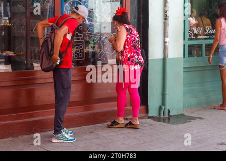 L'Avana, Cuba - 29 settembre 2023: Una donna cubana guarda in una vetrina di un negozio. Un uomo aspetta al suo fianco Foto Stock
