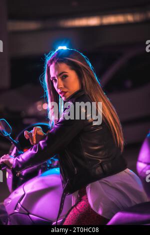 Fotografia con neon blu e rosa su una moto da dietro. Ritratto di una giovane modella bionda caucasica che indossa una giacca di pelle nera Foto Stock