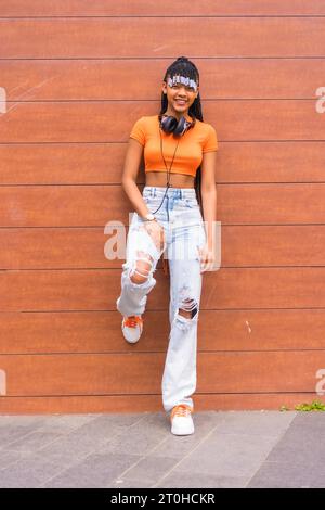 Stile di vita con una giovane ballerina in trappola in città. Ragazza di razza nera del gruppo etnico africano con maglietta arancione e pantaloni da cowboy Foto Stock