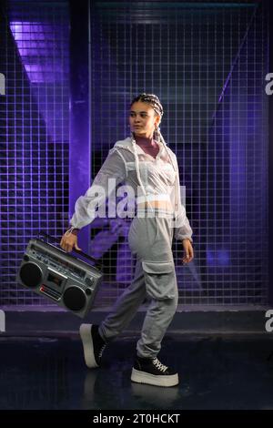 Giovane ragazza con trecce bianche con boombox su sfondo urbano, luci viola, stile 80s, fotografia retrò Foto Stock