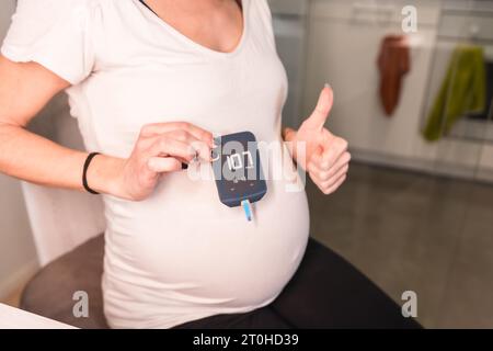 Giovane donna incinta che esegue un test di autodiagnosi del diabete gestazionale per controllare lo zucchero. Risultato positivo del test ematico Foto Stock