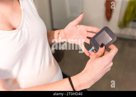 Giovane donna incinta che esegue un test di autodiagnosi del diabete gestazionale per controllare lo zucchero. La macchina canalizza lo zucchero nel sangue Foto Stock