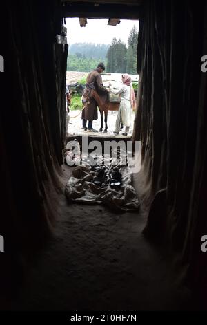 Una commovente scena si svolge a Yousmarg mentre un giovane Gujar abbraccia il suo lavoro quotidiano, e la sua devota sorella gli sta accanto, fornendo sostegno e amore incrollabili in un giorno di pioggia. Foto di Danish Showkat Foto Stock