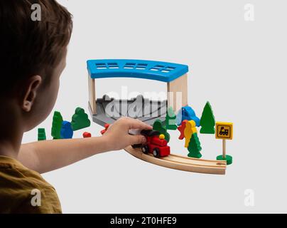 Ragazzo che gioca con i giocattoli. Trenino giocattolo per bambini con due automobili su una ferrovia di legno. Il deposito blu e gli alberi di Natale verdi completano il mondo dei giocattoli. Foto Stock