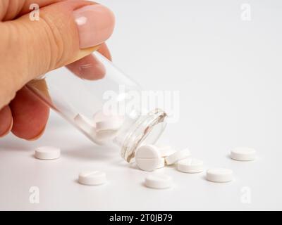 Primo piano di una donna che scuote pillole bianche dalla bottiglia di vetro su sfondo bianco. Concetto di trattamento medico con medicina o antidepressivi, salute Foto Stock