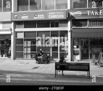 Una coppia più anziana di scooter mobili che mangia fuori da un ufficio di reclutamento delle forze a Peterborough Foto Stock