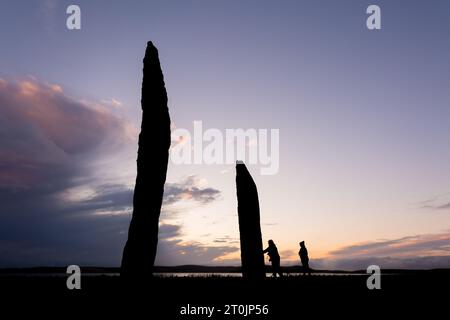 Stenness, Orcadi, Regno Unito. 7 ottobre 2023. Due turisti visitano le magnifiche pietre permanenti di Stenness al tramonto, nelle Orcadi, Regno Unito. Le enormi pietre di Stenness sono tutto ciò che rimane di un grande cerchio di pietre su un antico sito cerimoniale che risale a 5000 anni fa. Crediti: Peter Lopeman/Alamy Live News Foto Stock