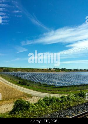 Un sistema di pannelli solari fotovoltaici su larga scala è situato nel mezzo di un campo erboso, con un cielo blu brillante sopra la testa Foto Stock