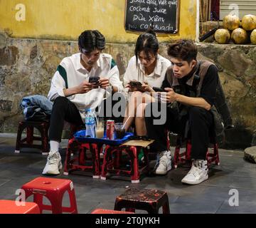 Hoi An, Vietnam. Tre giovani si sono immersi nei loro telefoni cellulari mentre bevevano qualcosa. Foto Stock