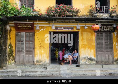 Hoi An, Vietnam. Fornitore di abbigliamento in attesa del primo cliente, la mattina presto. Foto Stock