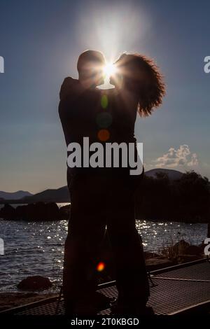 le sagome illuminano i raggi del sole al tramonto e si innamorano di un ponte sulla diga Foto Stock