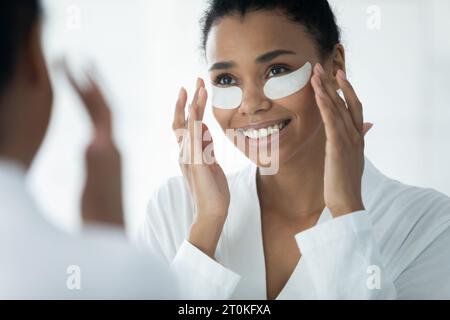La giovane donna birazziale si applica sotto i cerotti degli occhi in bagno Foto Stock