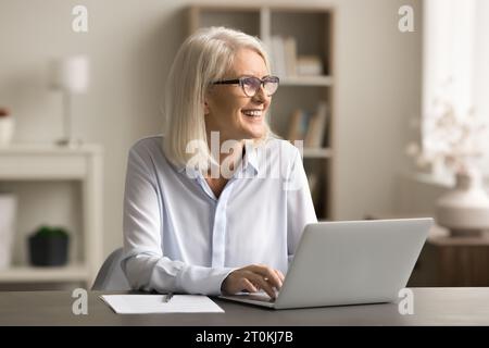 Positiva donna anziana freelancer bionda in occhiali che lavora a casa Foto Stock