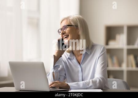 Donna d'affari anziana bionda positiva impegnata in una conversazione con il cellulare Foto Stock