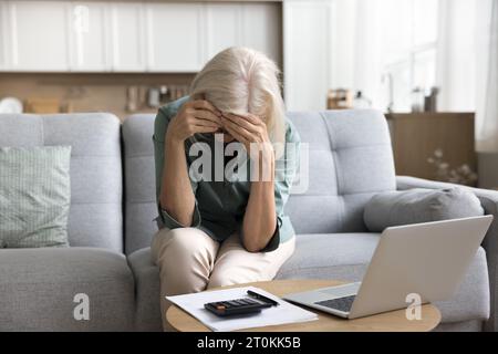 Frustrata donna anziana bionda stanca che tocca la testa alla calcolatrice Foto Stock