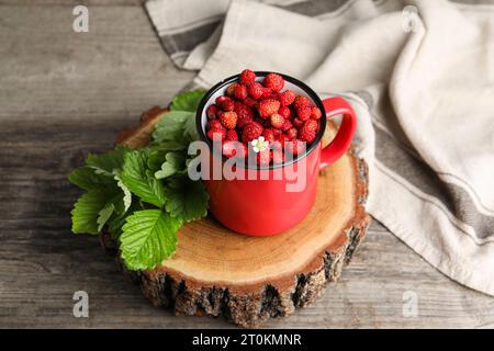 Fragole selvatiche fresche in tazza e foglie su tavola di legno Foto Stock