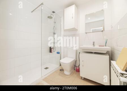 Bagno con comò in legno bianco e lavandino in porcellana bianca sotto uno specchio senza telaio Foto Stock