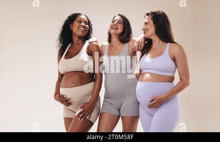 le donne incinte in abbigliamento fitness partecipano a una lezione di yoga, supportandosi a vicenda per tutto il terzo trimestre. Diversi gruppi di mamme che si allenano f Foto Stock