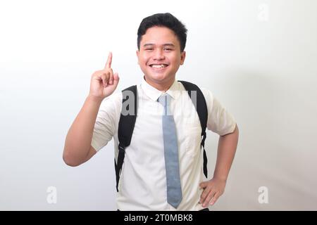 Studente indonesiano delle superiori che indossa un'uniforme bianca con cravatta grigia che punta verso l'alto con il dito e ricorda qualcosa da fare. Immagine isolata Foto Stock