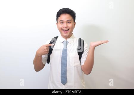 Studente delle superiori indonesiane che indossa un'uniforme bianca con cravatta grigia, sorride e guarda la macchina fotografica, mostrando qualcosa con le mani. ISOL Foto Stock