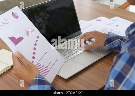 Primo piano della mano di un lavoratore freelance che lavora su un computer portatile e punta con il dito sui dati di analisi con grafico aziendale e diagra delle informazioni Foto Stock